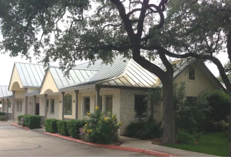 Two stone office buildings under oak trees in Helotes, Texas